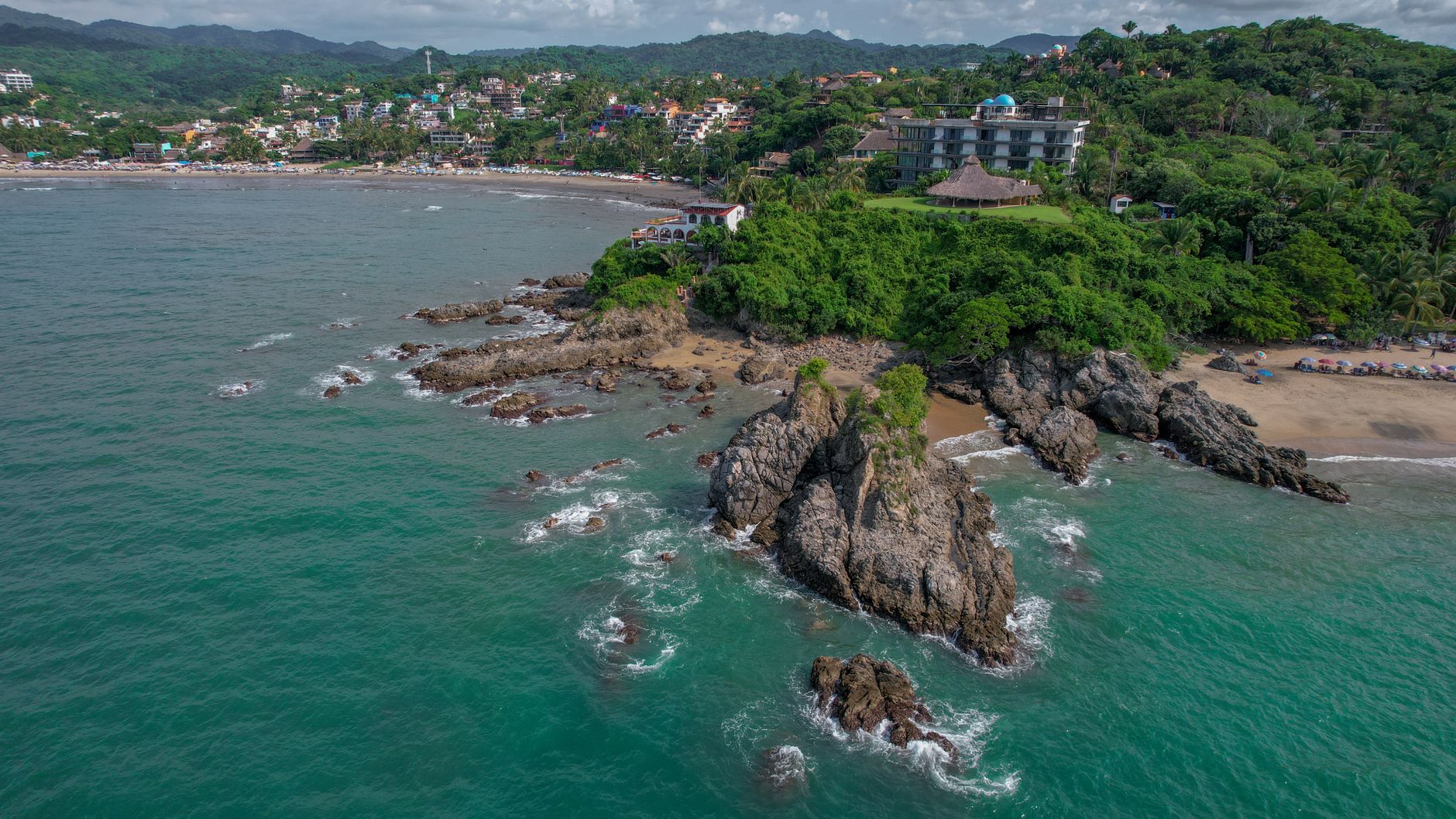 Playa de Sayulita, México, con palmeras y personas disfrutando del sol y el mar